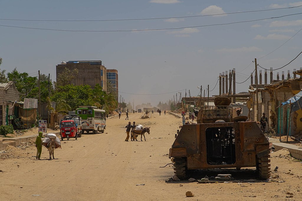 Hawzen dirt street, Ethiopia, with remains of bombed-out dwellings, destroyed type 89 AFV contrasted by mules carrying food.